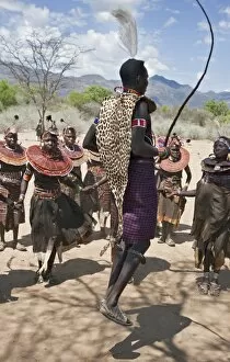 East Pokot District Collection: A Pokot warrior wearing a leopard skin jumps high in the air surrounded by women to celebrate an