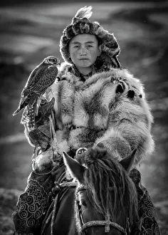Falcon Prints: Portrait of a Kazakh boy on horseback wearing traditional fur clothing and holding his pet falcon
