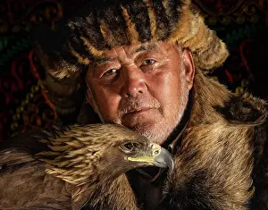 Mongolia Prints: Portrait of a Kazakh Eagle Hunter wearing traditional fur clothing and posing with his trained golden eagle