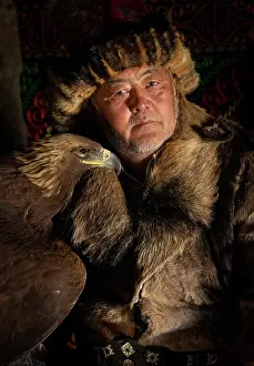 Mongolia Prints: Portrait of a Kazakh Eagle Hunter wearing traditional fur clothing and posing with his trained golden eagle