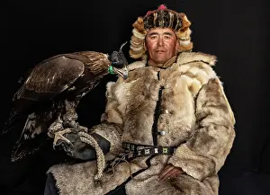 Mongolia Prints: Portrait of a Kazakh Eagle Hunter wearing traditional fur clothing and posing with his trained golden eagle