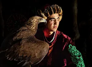 Mongolia Prints: Portrait of a young Kazakh Eagle Hunter wearing traditional fur clothing and posing with his trained golden eagle