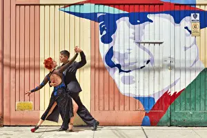 Dance Prints: Professional Tango Dancers in front of a wall art of the historical tango artist Carlos Gardel in the Abasto