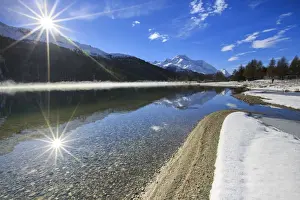 Snowy Peaks Prints: Rays of winter sun illuminate Lake Silvaplana still partially frozen Maloja Engadine
