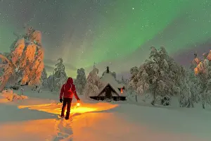 Rime Ice Prints: Rear a man with lantern admiring northern lights (aurora borealis) from a finnish hut (kota) in the icy forest