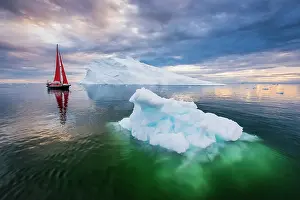 Danish Territory Prints: Red sailboat and blue iceberg at sunset in Disko Bay, Greenland