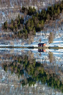 Timber Prints: Red timber hut (rorbu) and snowy hillside reflecting in flat calm water