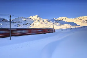 Highest Prints: The red train of Bernina whizzes through the snow at the Bernina pass at dawn. Engadine