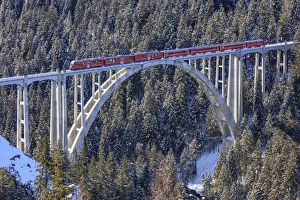 Red train of Rhaetian Railway on Langwies Viaduct surrounded by snowy woods Canton Red train of Rhaetian Railway on Langwies Viaduct surrounded by snowy woods Canton