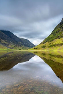 A Charnaich Collection: Reflections of mountains in Loch Achtriochtan in valley against cloudy sky, Glencoe