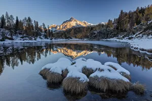 The rocky peak is reflected in the frozen Lake Mufule at dawn Malenco Valley province