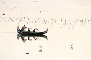 A rowing boat surrounded by birds carries two novice monks towards U-Bein bridge