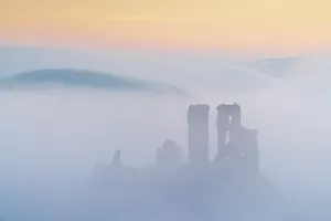 The ruins of Corfe Castle emerging from mist at dawn, Corfe Castle, Dorset, England. Winter (February) 2023