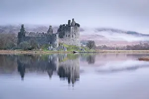The ruins of Kilchurn Castle reflected in Loch Awe at dawn on a misty morning in the Scottish Highlands, Argyll and Bute, Scotland. Winter (March) 2017