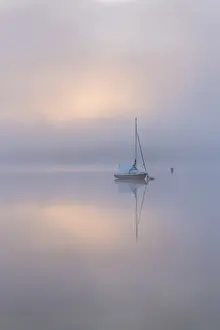 Sailing boat in misty conditions at dawn on a reflective Wimbleball Lake, Exmoor National Park