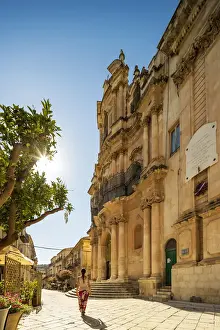 Baroque Style Prints: Scicli, Sicily. A woman walking in front of San Giovanni Evangelista church on a sunny