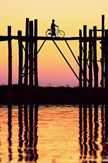 U Bein Prints: Silhouette of a person with a bicycle walking on the U-Bein wooden teak bridge at sunset