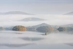 Single sculler rowing across a misty Derwent Water at dawn, Lake District, Cumbria, England