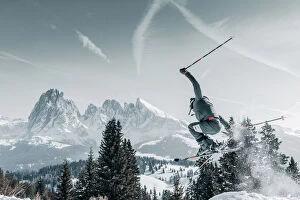 A skier jumping and raising snow with the Sassolungo in the background in the Alpe