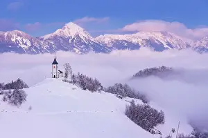 Slovenia, Jamnik, Church of St. Primoz sorrounded by fog at dusk with the Kamnik-Savinja Alps beyond, Gorenjska