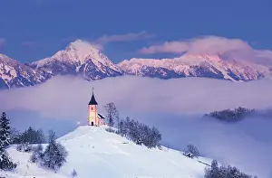 Slovenia, Jamnik, Church of St. Primoz sorrounded by fog at dusk with the Kamnik-Savinja Alps beyond, Gorenjska