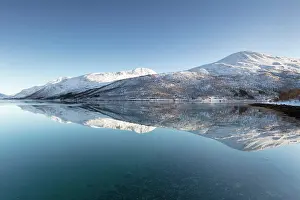 Troms Prints: Snow-covered mountains with a perfect reflection in flat calm waters of a fjord