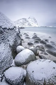 Fiord Prints: Snow covered rocks on the beach modeled by the wind surround the icy sea Pollen Vareid
