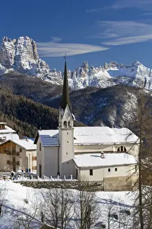 The snowy alpine village and church of Zoppa di Cadore framed by the peak of Bosconero