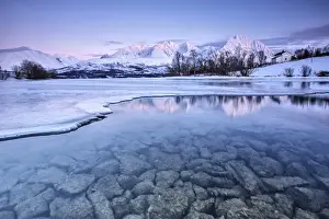 Snowy peaks are reflected in the frozen Lake Jaegervatnet at sunset Stortind Lyngen Alps Tromsa¸ Lapland Norway Europe