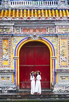 Images Dated 17th March 2020: Southeast Asia, Vietnam, Hue. Two young women wearing Ao Dai dresses stand next to an