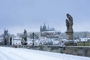 Statues at snow-covered Charles bridge and Prague Castle in winter, Prague, Bohemia