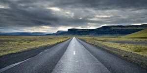 Straight empty road leading towards mountains against cloudy sky, South Iceland, Iceland
