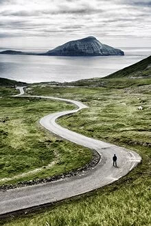 One Person Collection: Stremnoy island, Faroe Islands, Denmark. Man standing on a bending road. (MR)