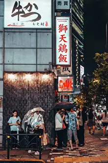 Shop Prints: Summer night in Tokyo, Japan. People wait in line to enter the restaurant under the rain and illuminated signs