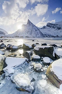 Climate Collection: Sun rays over Hatten mountain peak overlooking the frozen sea, Ersfjord beach, Senja island