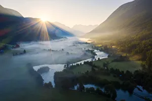 Sun Ray Prints: Sunburst during a foggy sunrise over Stryneelva river and fields, aerial view, Stryn
