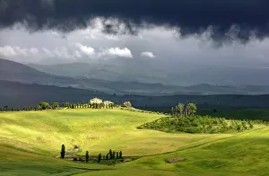 Pienza Prints: Sunlit farmhouse and green fields beneath a dark