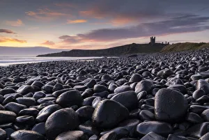 Images Dated 8th December 2021: Sunrise over Dunstanburgh Castle from the black boulder shore of Embleton Bay