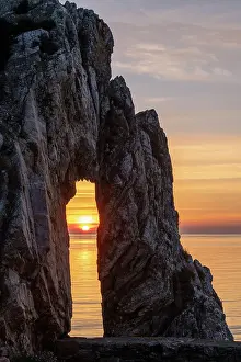 Sunrise through a rock arch at the Victorian brickworks site at Porth Wen, Anglesey, Wales, UK. Spring (May) 2019