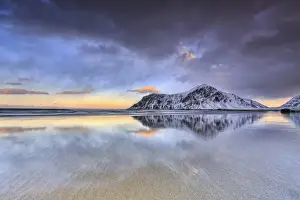 Sunset on Skagsanden beach surrounded by snow covered mountains reflected in the cold sea
