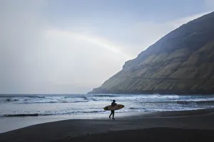 Black Sand Prints: A surfer walking along the beach in Tjornuvik. Streymoy, Faroe Islands