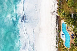 Crystal Collection: Swimming pool of a tourist resort on white coral beach washed by waves, overhead view, Zanzibar