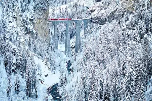 Railway Track Prints: Swiss red train crossing Landwasser viaduct above a frozen river in the snowy landscape