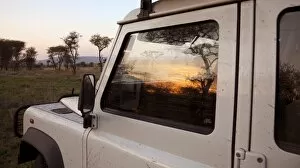 Bushman Gallery: Tanzania, Serengeti. Sunrise over the bush is reflected in the window of a Land Rover