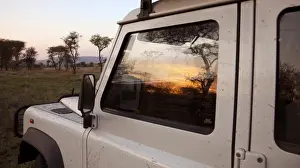 Jeep Prints: Tanzania, Serengeti. Sunrise over the bush is reflected in the window of a Land Rover
