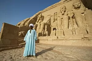 A temple guardian stands in front of the facade of Abu Simbel