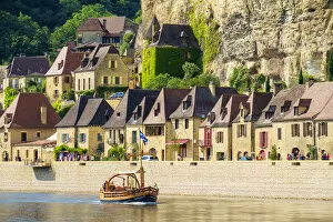 Tourist boat passing in front of old stone houses on Dordogne River in late afternoon