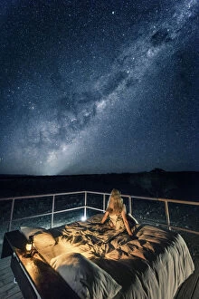 Tourist sitting on a bed outdoor admiring the stars of the Southern Hemisphere, Namibia, Africa