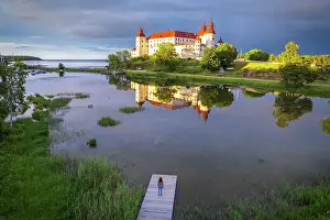 Fortified Wall Prints: One tourist standing on the river of Vanem lake admires Lacko castle at sunset