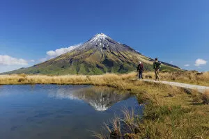 Two tourists hiking at Taranaki volcano in New Zealand northern island reflecting in a